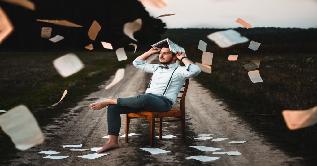 How to counter straw man argument - man sitting in chair in middle of countryside road, books are flying from sky, man shielding his head with open book - fallaciesoflogic.com